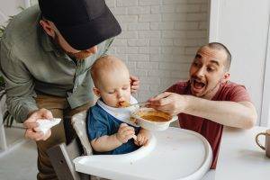 Man in Red Shirt Feeding Baby on a High Chair