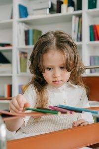 Photograph of a Child with Brown Hair Arranging Colored Pencils
