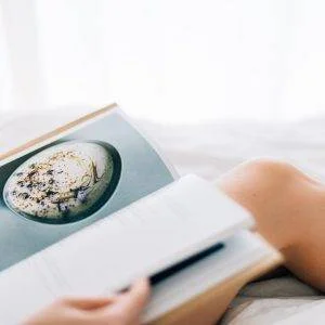 person holding open magazine while laying on bed