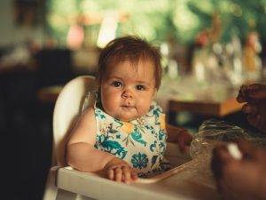 Baby in White Green and Yellow Floral Bib Sitting on High Chair